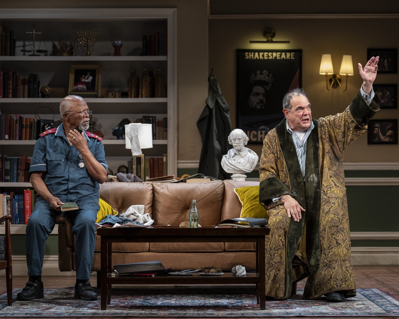 Edward Gero as Jack Morris, arm raised mid-speech, with John Kani as Lunga Kunene seated on the sofa